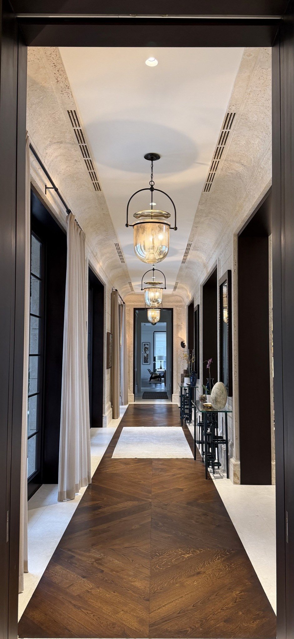Vaulted travertine-finish hallway with lantern pendants and chevron wood floor by Kim Delaney, Delaney Fine Finishes